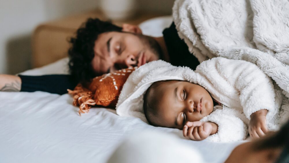 Father and infant peacefully sleeping together in bed, creating a heartwarming and bonding moment.